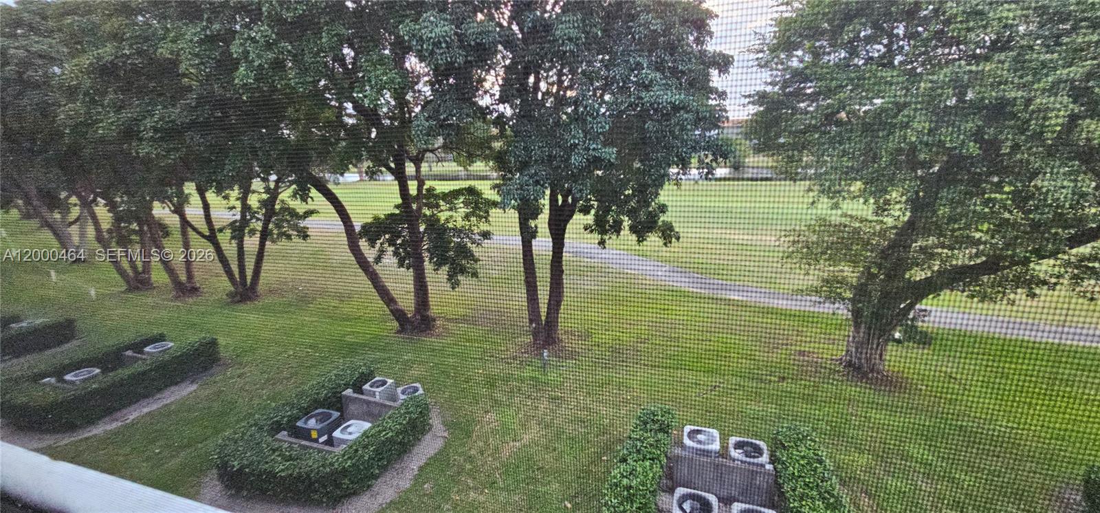 A view from a window looking out over a grassy lawn, trees, and a path — PEMBROKE PINES, FL