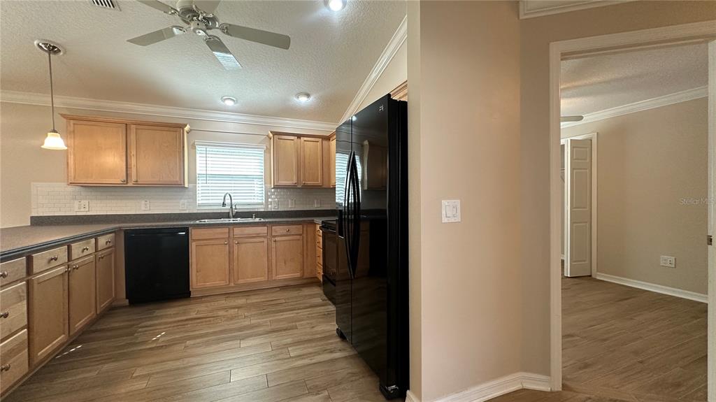 A kitchen with light wood cabinets, dark countertops, and a black refrigerator faces an entryway — 724 YAGER LANE, THE VILLAGES, FL