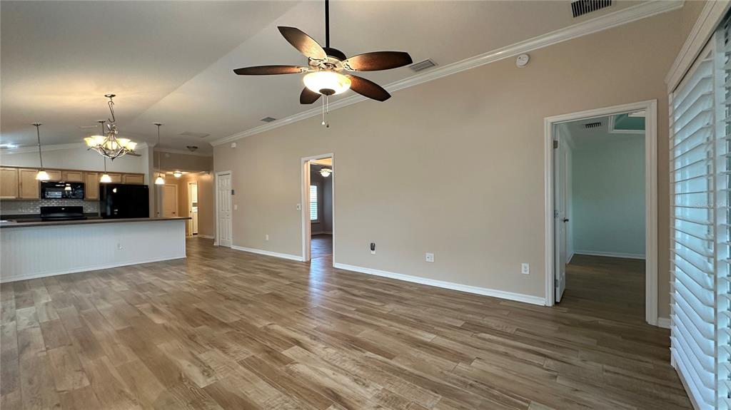A spacious living area features wood-look flooring, a ceiling fan, and an open kitchen — 724 YAGER LANE, THE VILLAGES, FL
