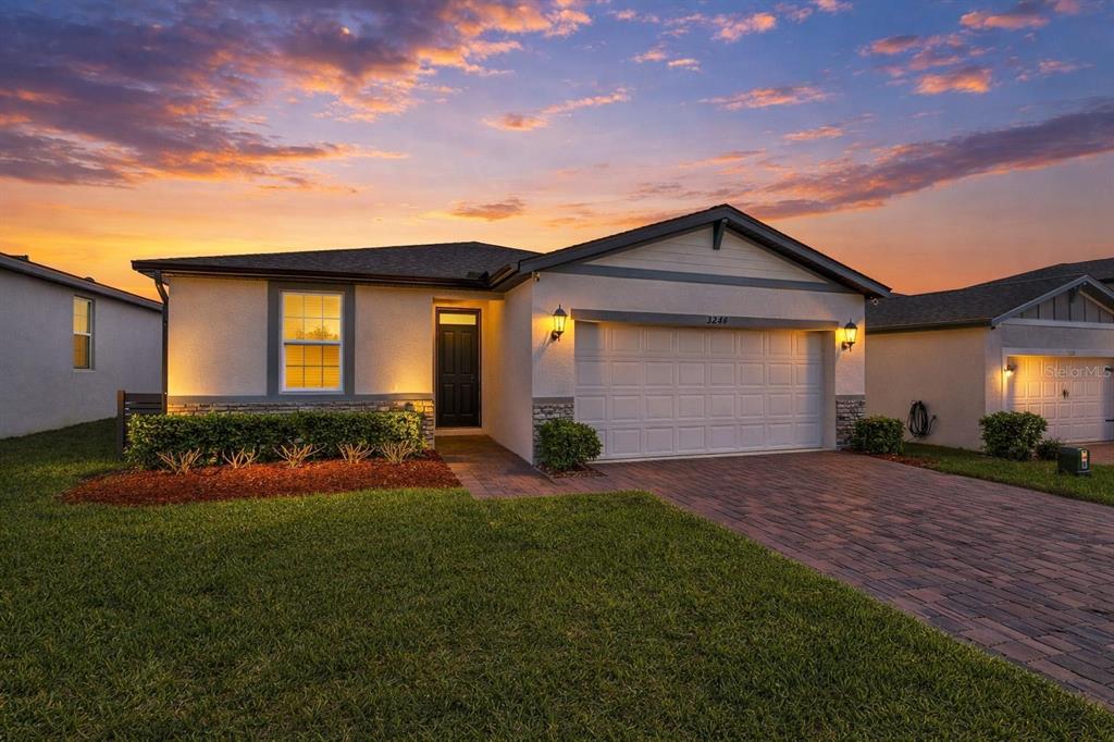 A single-story house with a paved driveway, a two-car garage, and a sunset sky — 3224 WEITZEL DRIVE, HAINES CITY, FL