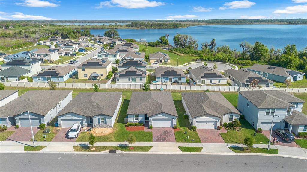 An aerial view shows a suburban neighborhood with houses featuring solar panels near a lake — 3224 WEITZEL DRIVE, HAINES CITY, FL