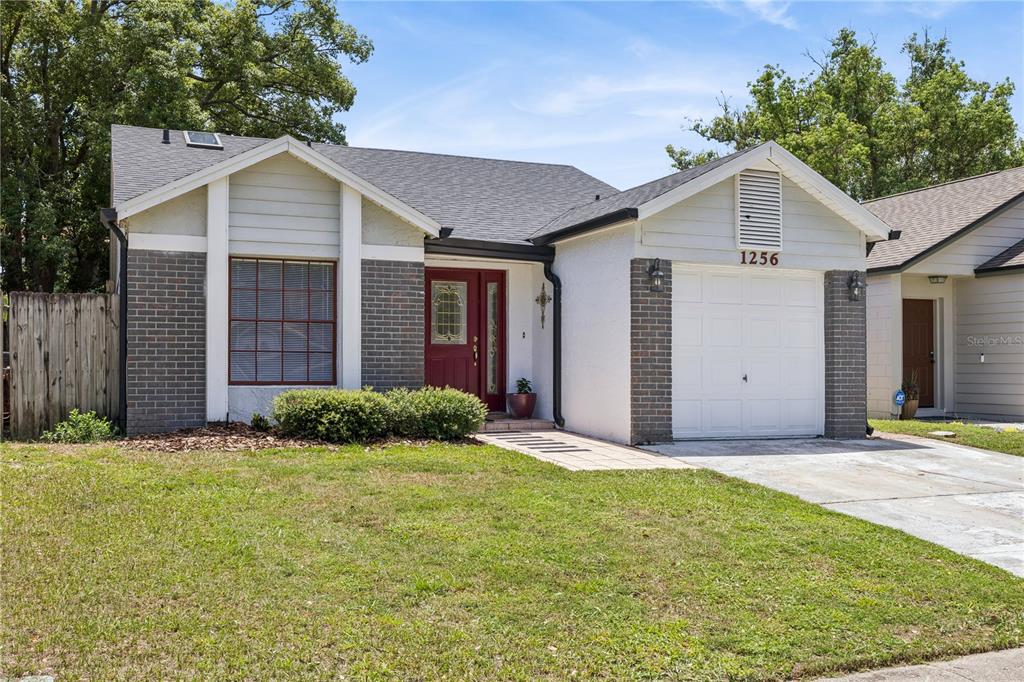 A single-story house with a brick and stucco exterior, a red front door, and a garage — 1256 PIN OAK DRIVE, APOPKA, FL
