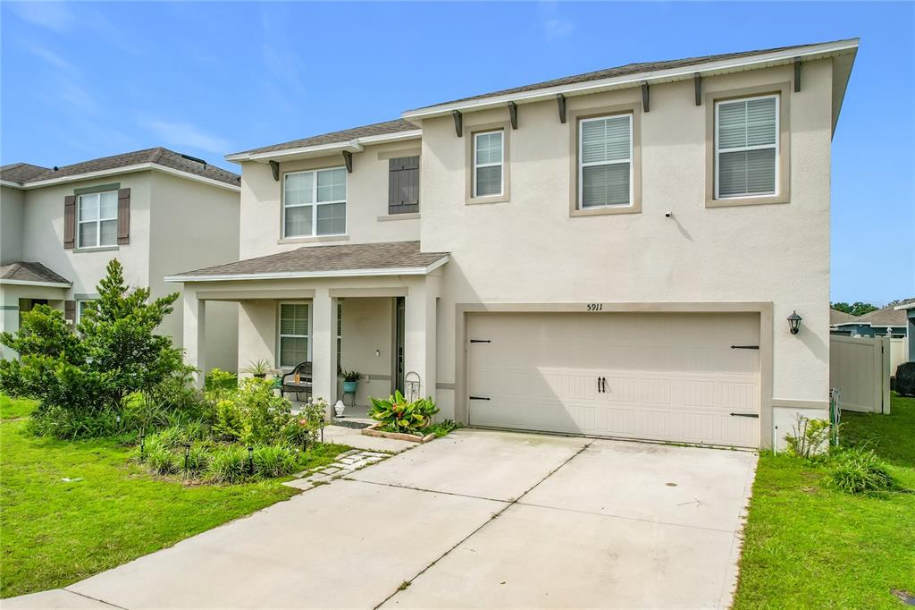 A two-story suburban house with a beige stucco exterior, a two-car garage, and a driveway — 5911 SHINGLE CREEK ROAD, LAKELAND, FL