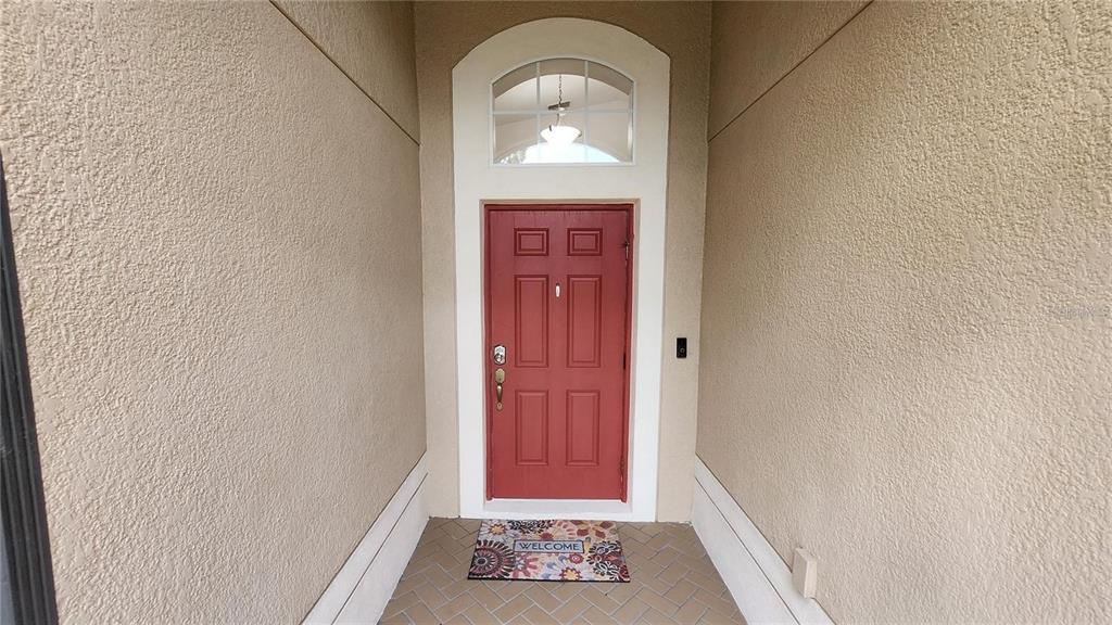 A red front door with a transom window sits at the end of a covered entryway — 11404 HOLMBRIDGE LANE, RIVERVIEW, FL