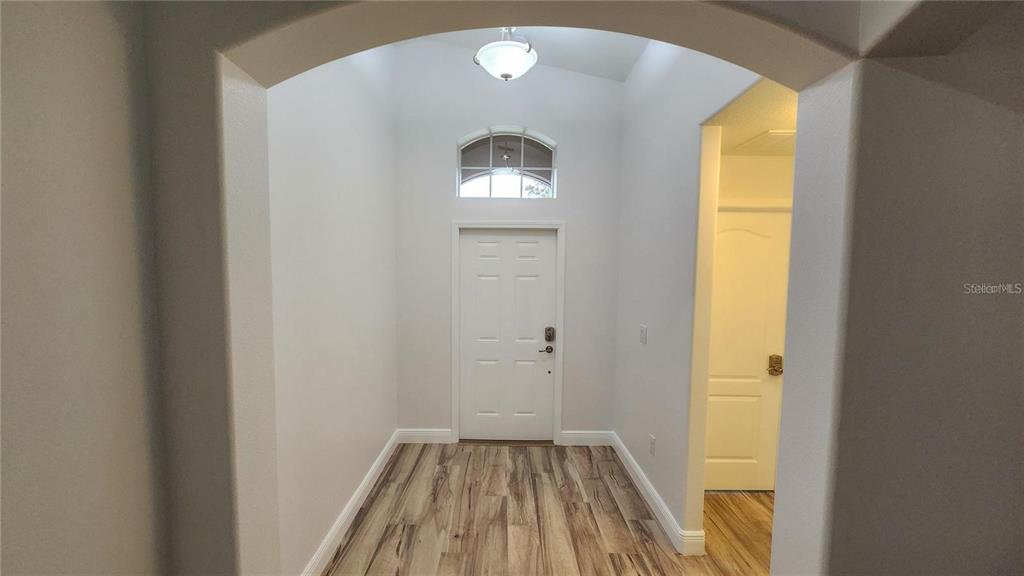 A bright entryway features light-colored walls, wood-look flooring, a white front door, and arched architecture — 11404 HOLMBRIDGE LANE, RIVERVIEW, FL
