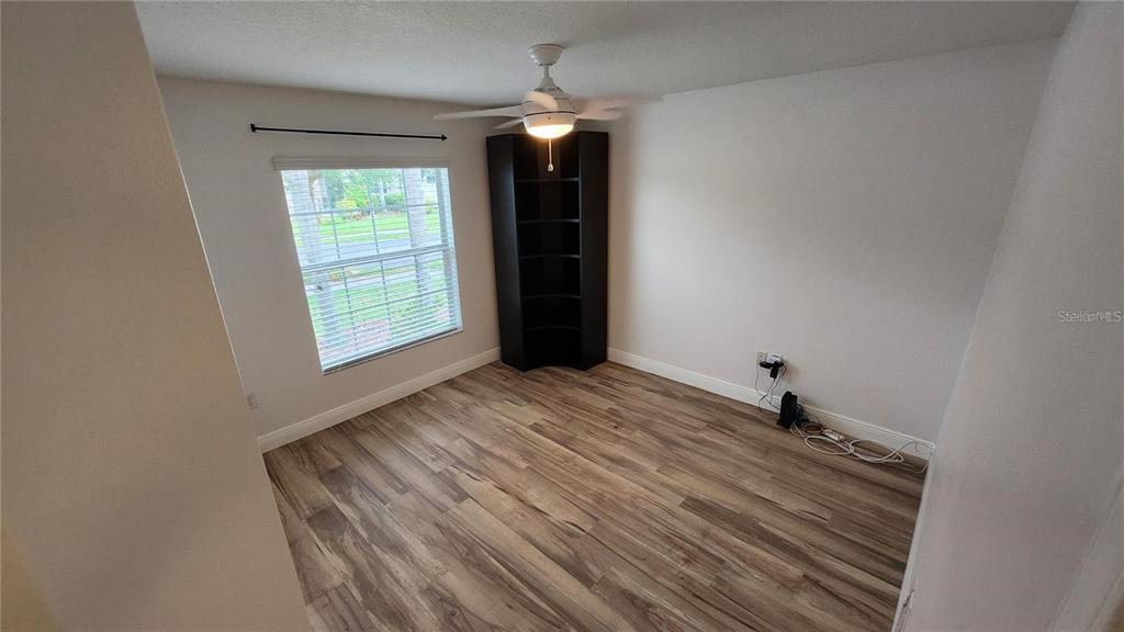 A bedroom with wood-look flooring, a ceiling fan, a corner bookshelf, and a window — 11404 HOLMBRIDGE LANE, RIVERVIEW, FL