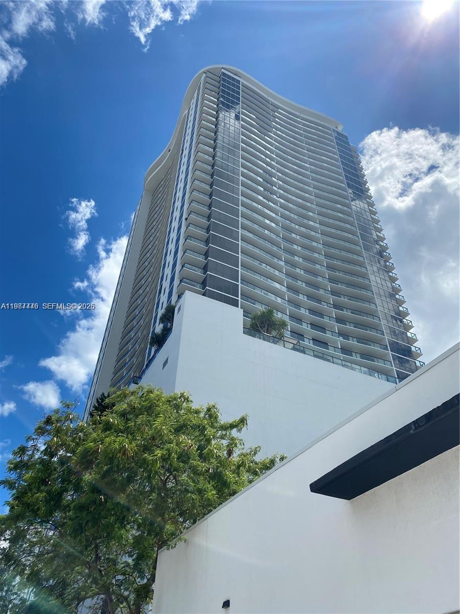 A low-angle view of a tall, modern residential skyscraper with glass balconies against a blue sky — 1600 NE 1st Ave # 1715, Miami FL 33132, MIAMI, FL