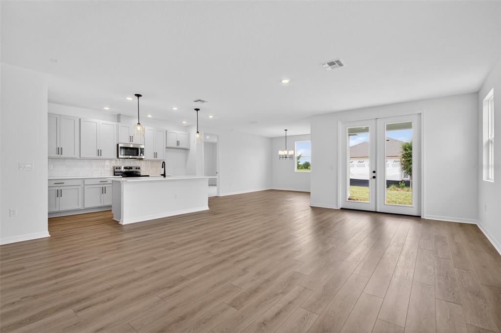 A bright, open-concept kitchen and living area with light wood floors and white cabinetry — 30157 MISTY PINES ROAD, MOUNT DORA, FL