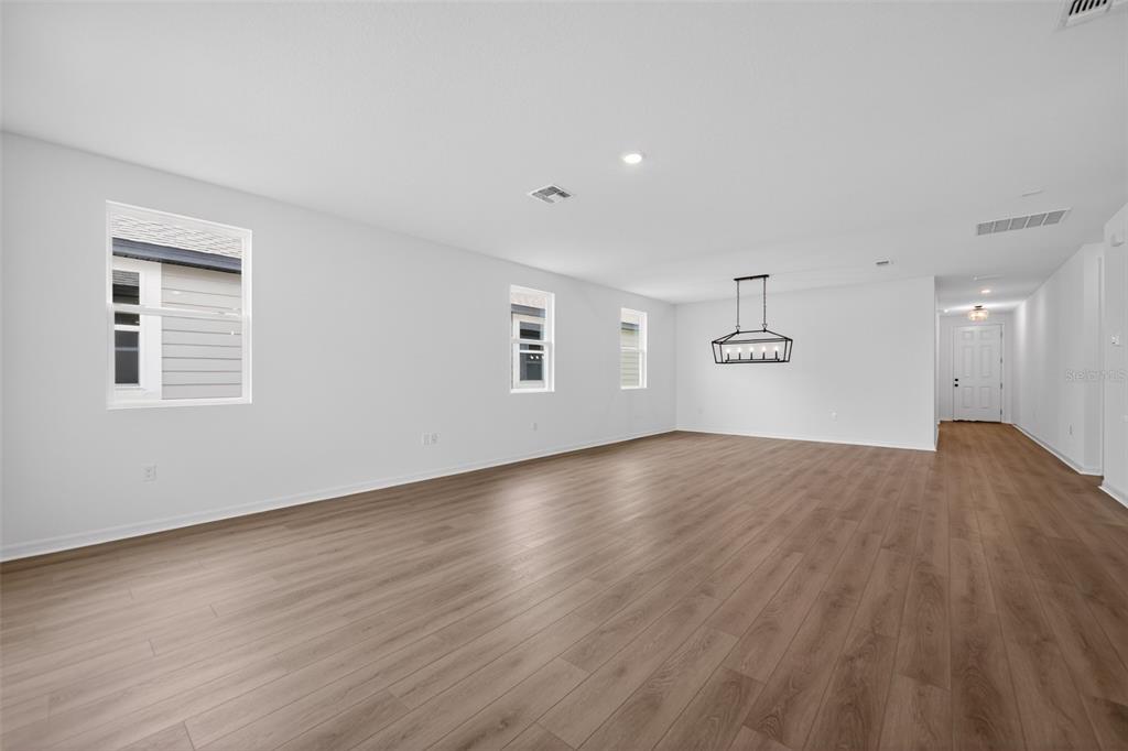 An empty living room with light wood-look flooring, white walls, and a modern chandelier — 30157 MISTY PINES ROAD, MOUNT DORA, FL