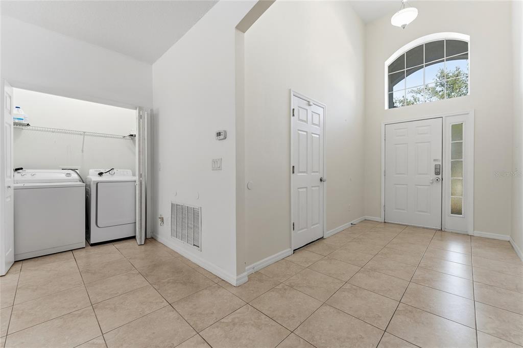 An entryway with tile flooring, a high ceiling, a front door, and an open laundry closet — 4704 BLUE DIAMOND STREET, KISSIMMEE, FL