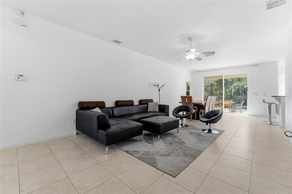 A living room with a black sectional sofa, tiled floors, and a sliding glass door — 4704 BLUE DIAMOND STREET, KISSIMMEE, FL