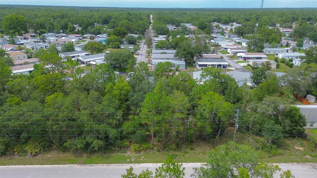 An aerial view shows a wooded, undeveloped lot situated in front of a residential neighborhood — 6859 W MERRIVALE LANE, HOMOSASSA, FL