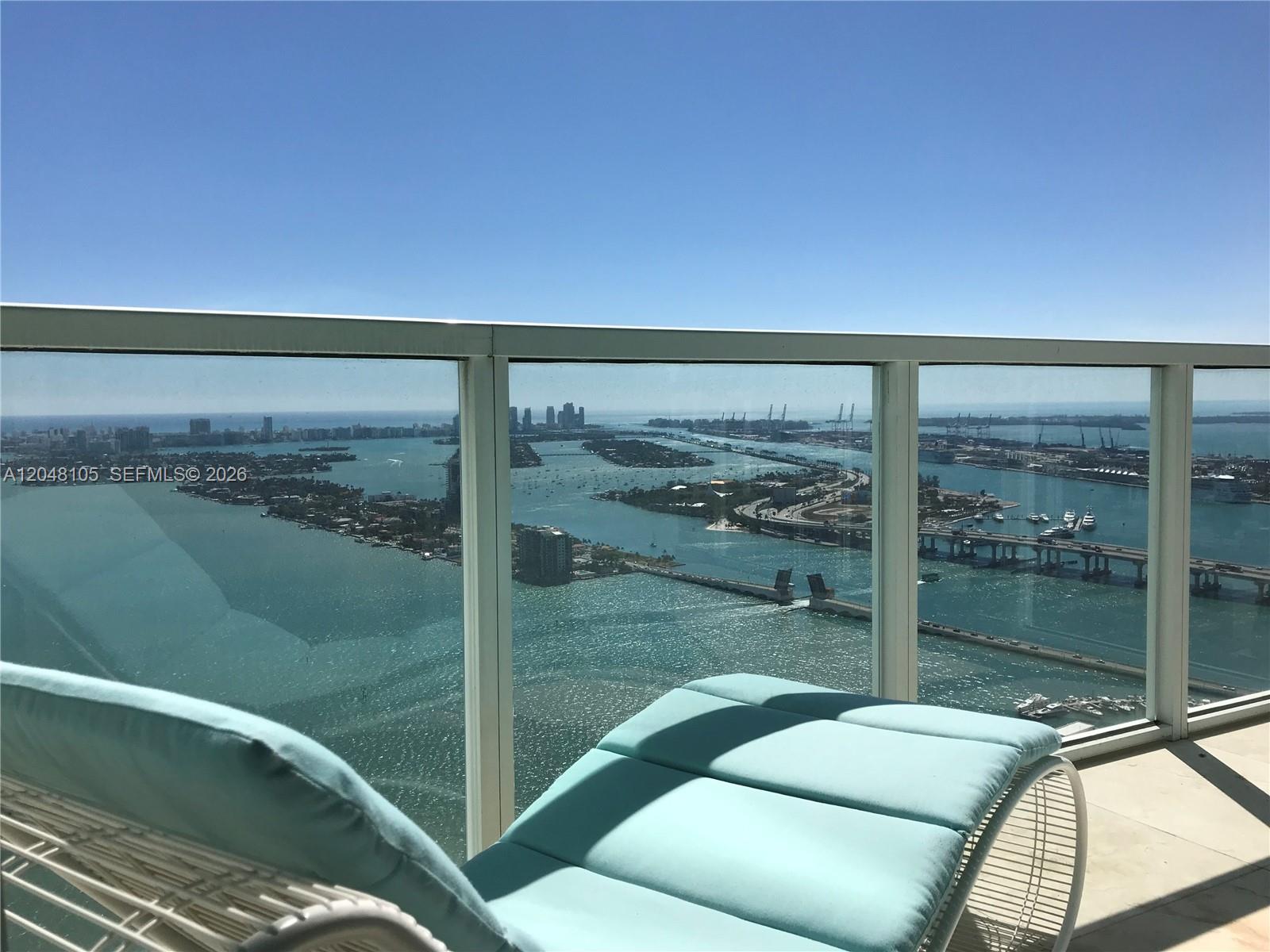 A balcony with a lounge chair overlooks a bay, bridges, and a distant city skyline — 1900 N Bayshore Dr # 5003, Miami FL 33132, MIAMI, FL