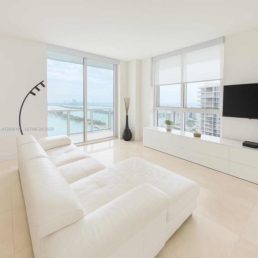 A modern living room features a white sectional sofa, floor-to-ceiling windows, and water views — 1900 N Bayshore Dr # 5003, Miami FL 33132, MIAMI, FL