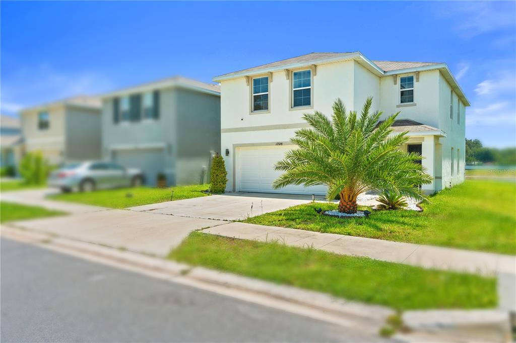 A two-story house with a white exterior, a two-car garage, and a palm tree — 13576 WHISKEY DAISY DRIVE, DADE CITY, FL
