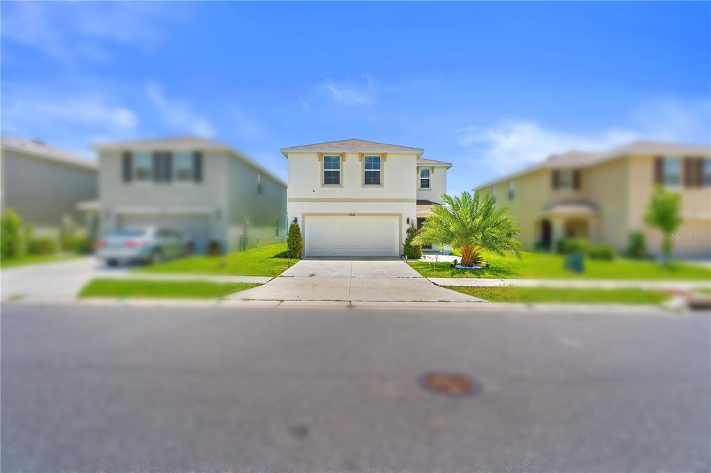 A two-story suburban house with a two-car garage and a palm tree in front — 13576 WHISKEY DAISY DRIVE, DADE CITY, FL