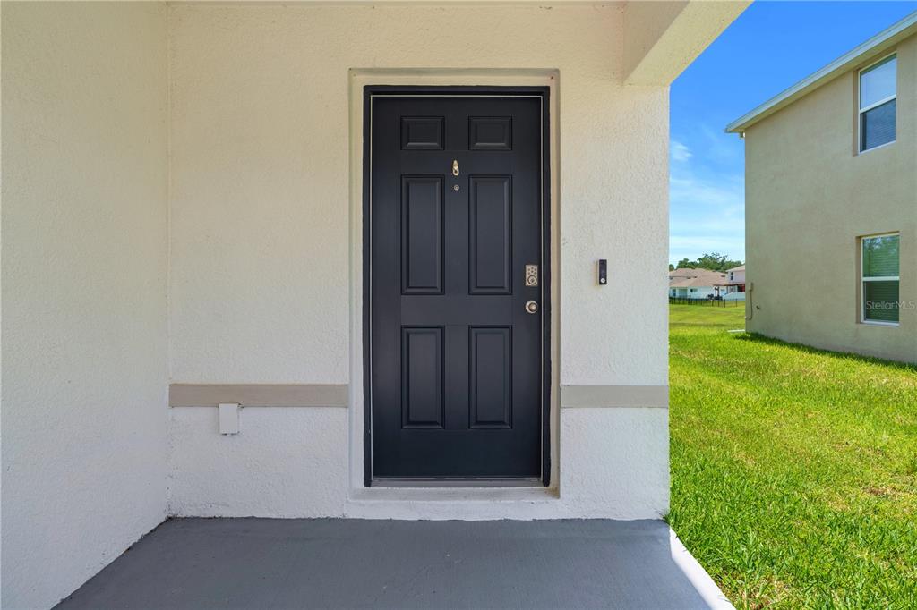 A dark front door with a peephole is centered on a covered concrete porch — 13576 WHISKEY DAISY DRIVE, DADE CITY, FL
