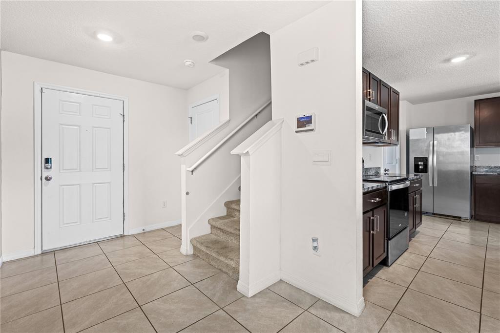 An entryway with tile flooring leads to a carpeted staircase next to a modern kitchen — 13576 WHISKEY DAISY DRIVE, DADE CITY, FL