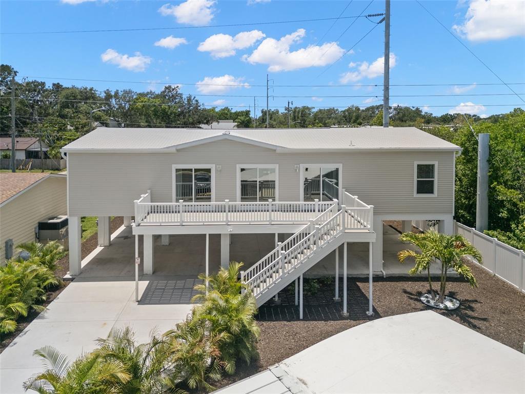 An elevated house with light siding, a large deck, and stairs leading to the ground level — 6924 AMERICANA DRIVE NE UNIT 167, ST PETERSBURG, FL