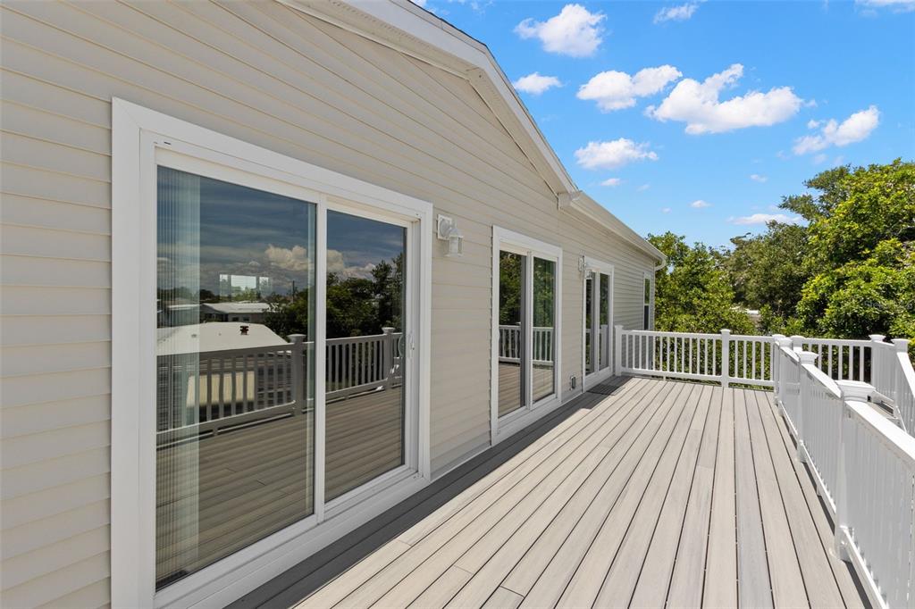 A wide wooden deck with white railings sits outside a house with sliding glass doors — 6924 AMERICANA DRIVE NE UNIT 167, ST PETERSBURG, FL