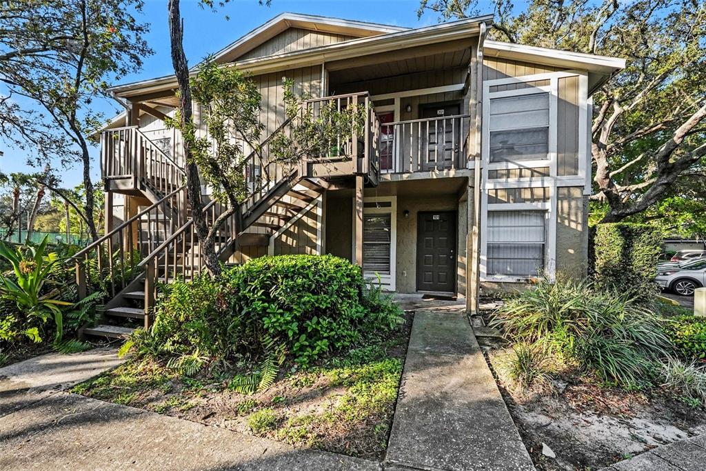 A two-story apartment building with tan siding, a wooden staircase, and a concrete walkway — 14319 HANGING MOSS CIRCLE UNIT 101, TAMPA, FL