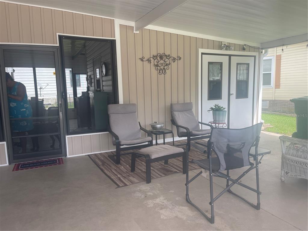 A covered patio features a rug, outdoor chairs, a small table, and a storage shed door — 112 LYONIA LANE, WILDWOOD, FL