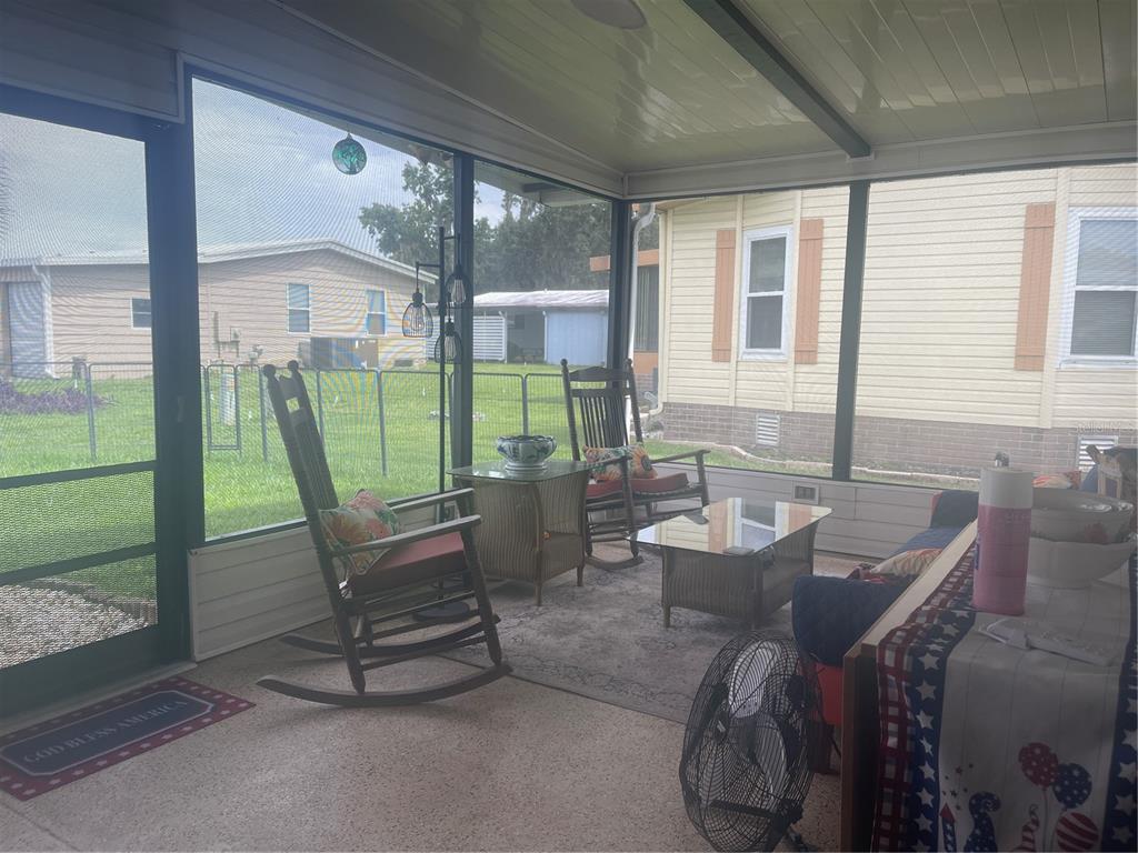 A screened-in porch features rocking chairs, a coffee table, and views of neighboring houses — 112 LYONIA LANE, WILDWOOD, FL