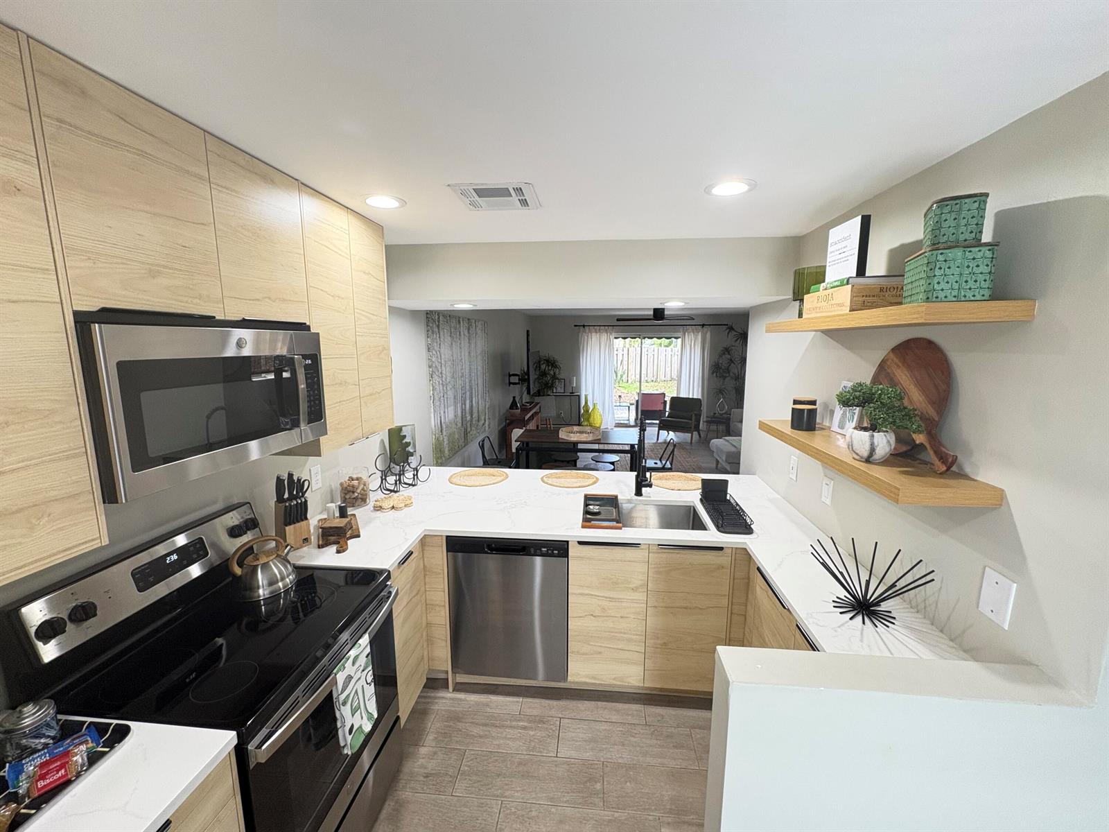 A modern kitchen features light wood cabinets, stainless steel appliances, and open shelving — 690 SE 23rd Avenue # 1, Pompano Beach FL 33062, POMPANO BEACH, FL