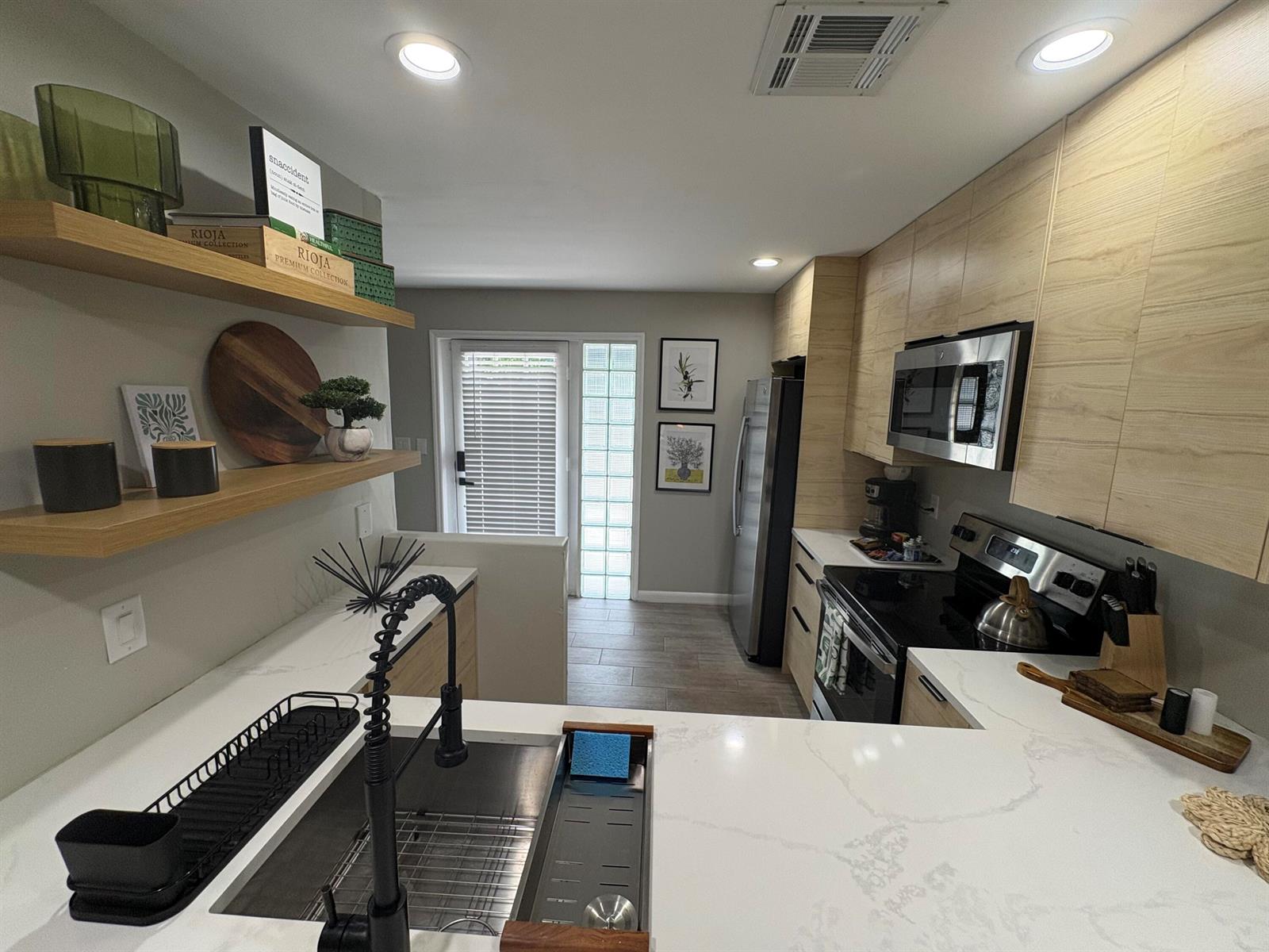 A modern kitchen features light wood cabinets, white quartz countertops, open shelving, and stainless appliances — 690 SE 23rd Avenue # 1, Pompano Beach FL 33062, POMPANO BEACH, FL