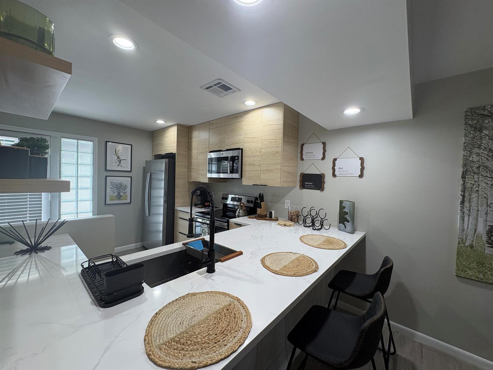 A modern kitchen features light wood cabinets, white quartz countertops, and black bar stools — 690 SE 23rd Avenue # 1, Pompano Beach FL 33062, POMPANO BEACH, FL