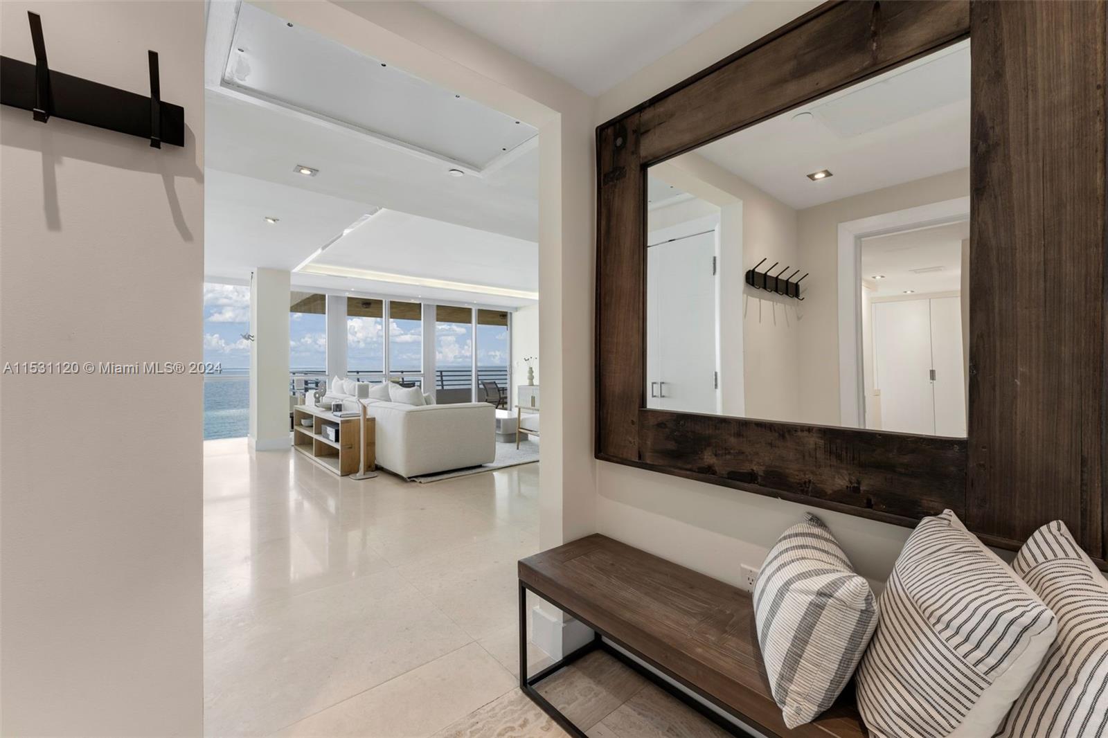 A foyer with a wooden bench and mirror opens into a bright living room overlooking water — 101 Ocean Dr # 907, Miami Beach FL 33139, MIAMI BEACH, FL