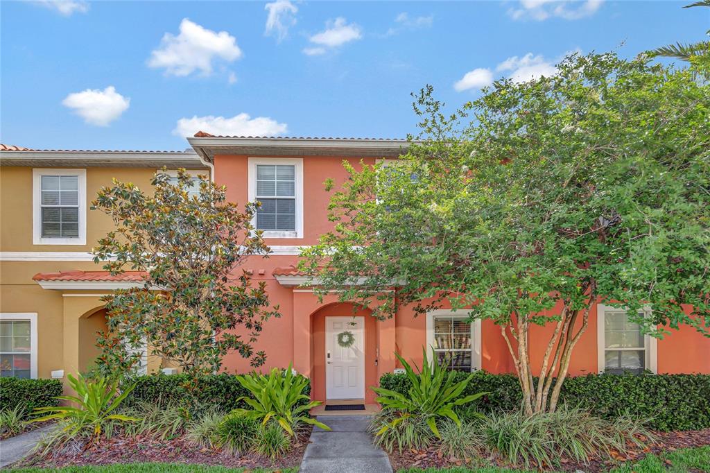 A two-story townhouse with a coral-colored stucco exterior, a white front door, and landscaping — 3050 WHITE ORCHID ROAD, KISSIMMEE, FL