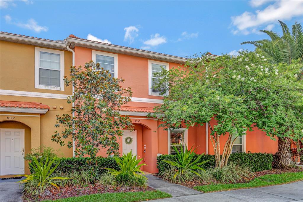 The exterior of two adjacent townhomes features orange and tan stucco walls with white trim — 3050 WHITE ORCHID ROAD, KISSIMMEE, FL