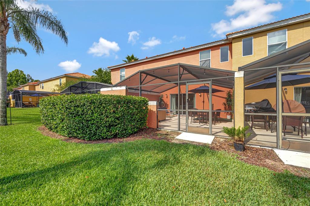 A backyard view of a two-story house with a screened-in patio and green lawn — 3050 WHITE ORCHID ROAD, KISSIMMEE, FL