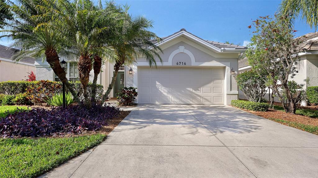 A single-story house features a concrete driveway, a two-car garage, and a palm tree — 6716 SPRING MOSS PLACE, LAKEWOOD RANCH, FL