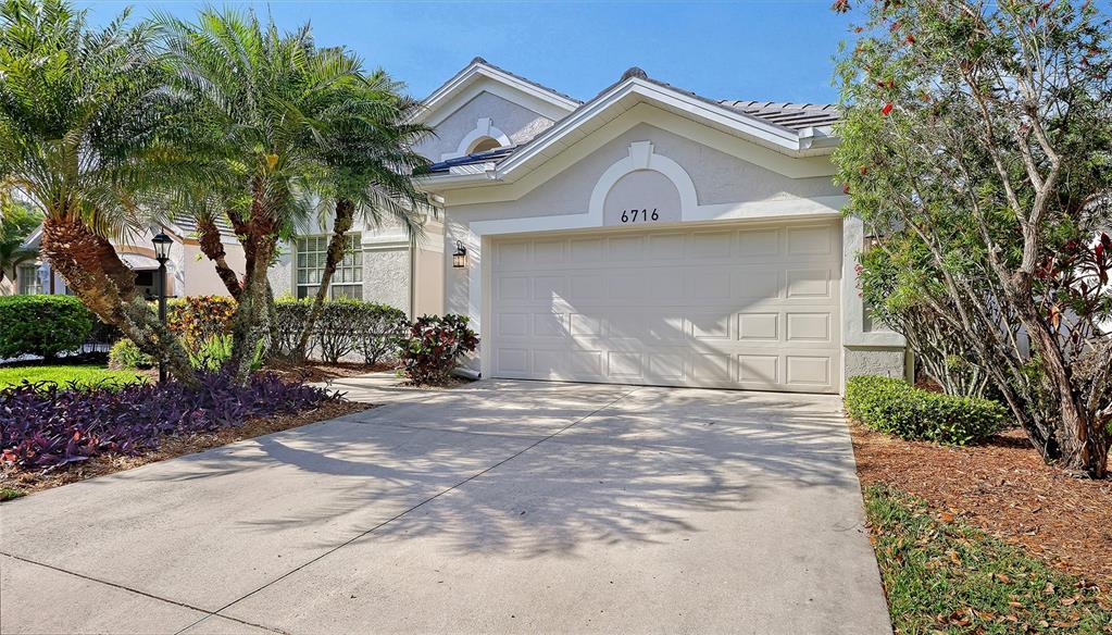 A single-story house with a beige stucco exterior, a two-car garage, and palm trees — 6716 SPRING MOSS PLACE, LAKEWOOD RANCH, FL