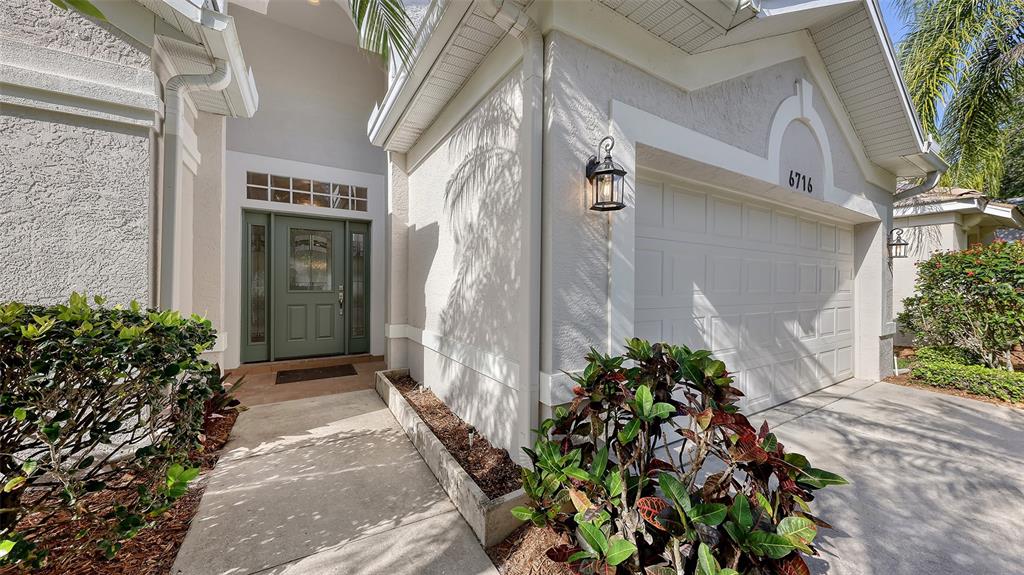 The exterior of a house features a white garage, a green front door, and landscaping — 6716 SPRING MOSS PLACE, LAKEWOOD RANCH, FL