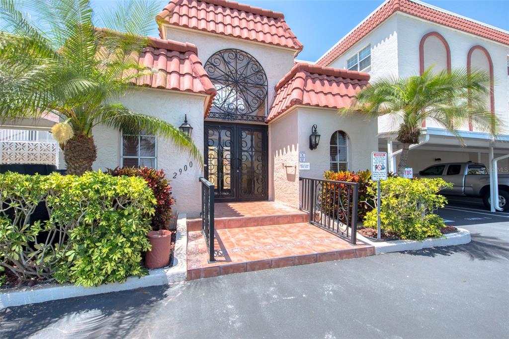 The exterior of a building features a tiled roof, arched metal doors, and a palm tree — 2900 GULF BOULEVARD UNIT 211, BELLEAIR BEACH, FL