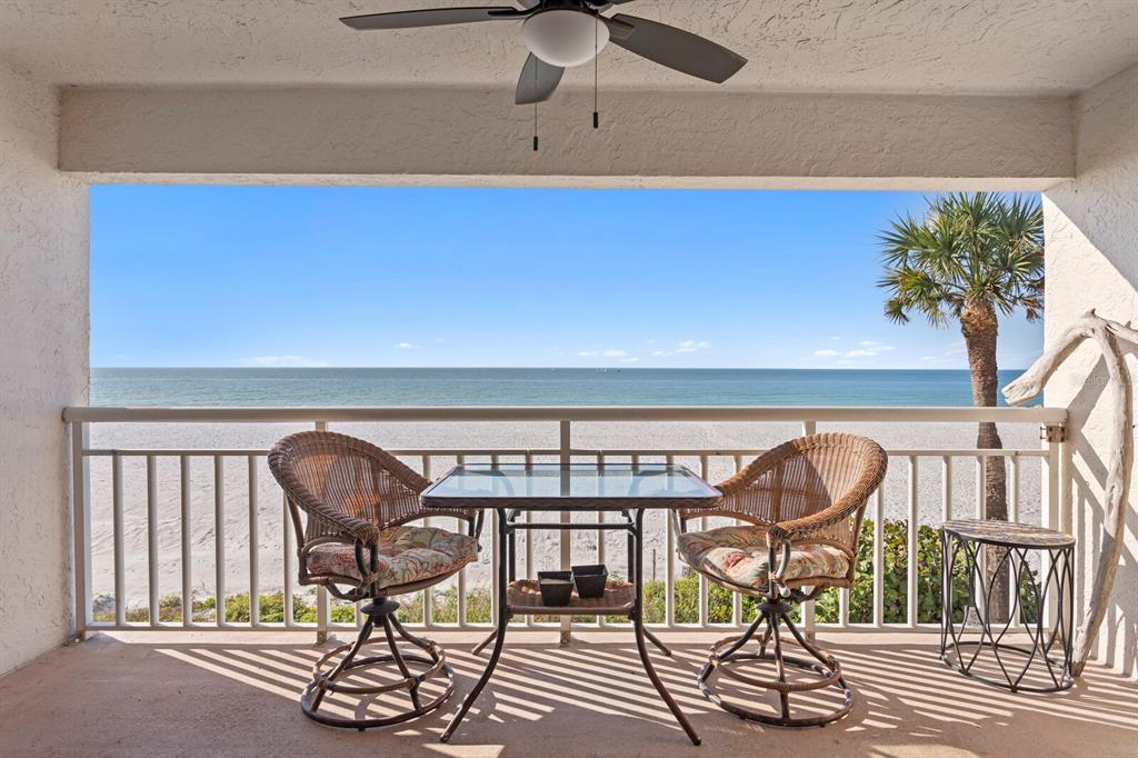 A balcony with a table and two chairs overlooks a sandy beach and the ocean — 2900 GULF BOULEVARD UNIT 211, BELLEAIR BEACH, FL