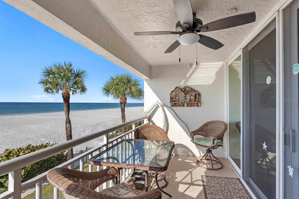 A balcony with wicker furniture and a ceiling fan overlooks a sandy beach and ocean — 2900 GULF BOULEVARD UNIT 211, BELLEAIR BEACH, FL