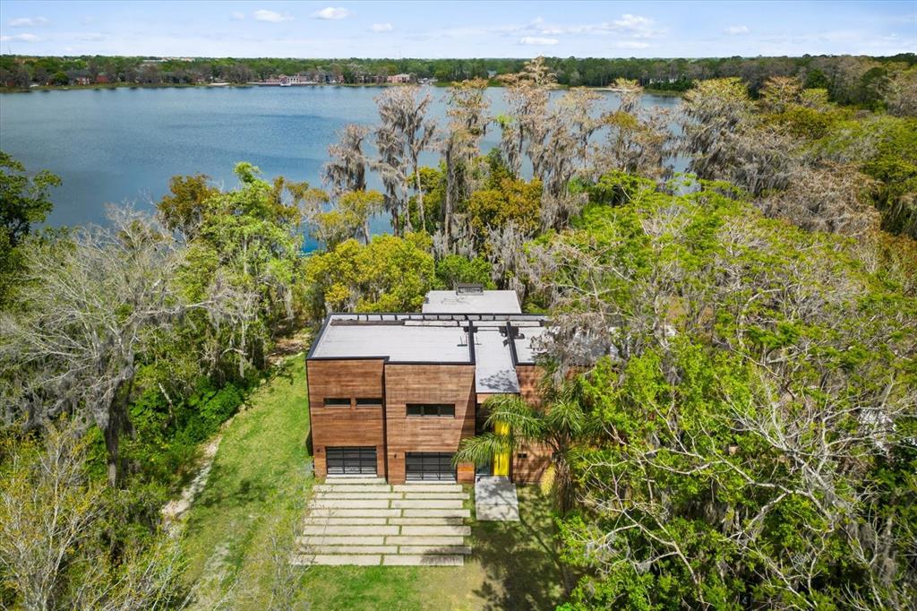 An aerial view of a modern wood-paneled house situated on a lakefront lot with trees — 3807 S SEMORAN BOULEVARD, ORLANDO, FL