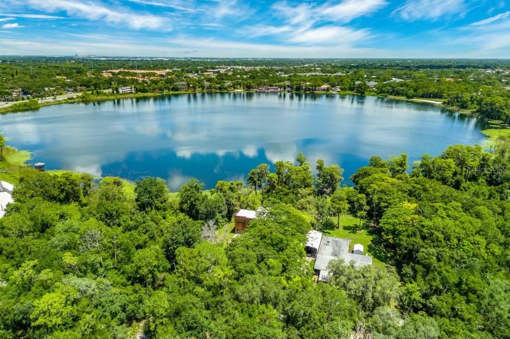An aerial view shows a house nestled in a wooded area beside a large lake — 3807 S SEMORAN BOULEVARD, ORLANDO, FL