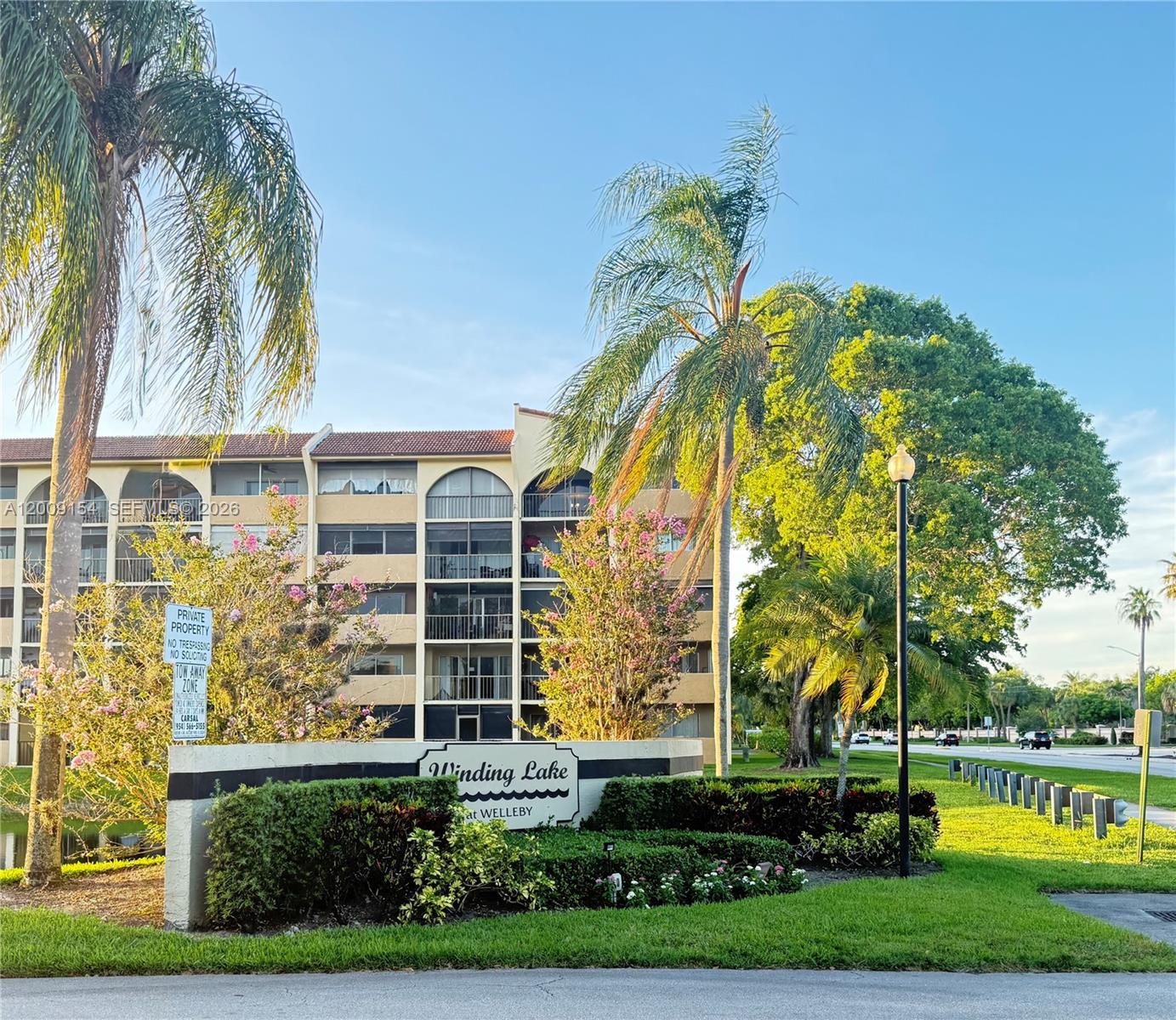 The exterior of a multi-story apartment building features a Winding Lake at Welleby entrance sign — 10016 Winding Lake Rd # 202, Sunrise FL 33351, SUNRISE, FL