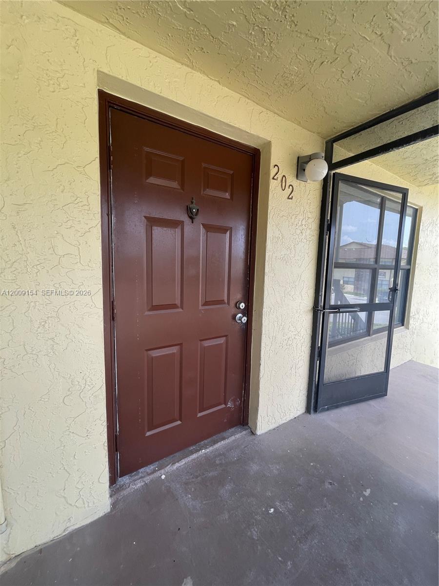 A brown front door with a door knocker is labeled with the number 202 — 10016 Winding Lake Rd # 202, Sunrise FL 33351, SUNRISE, FL