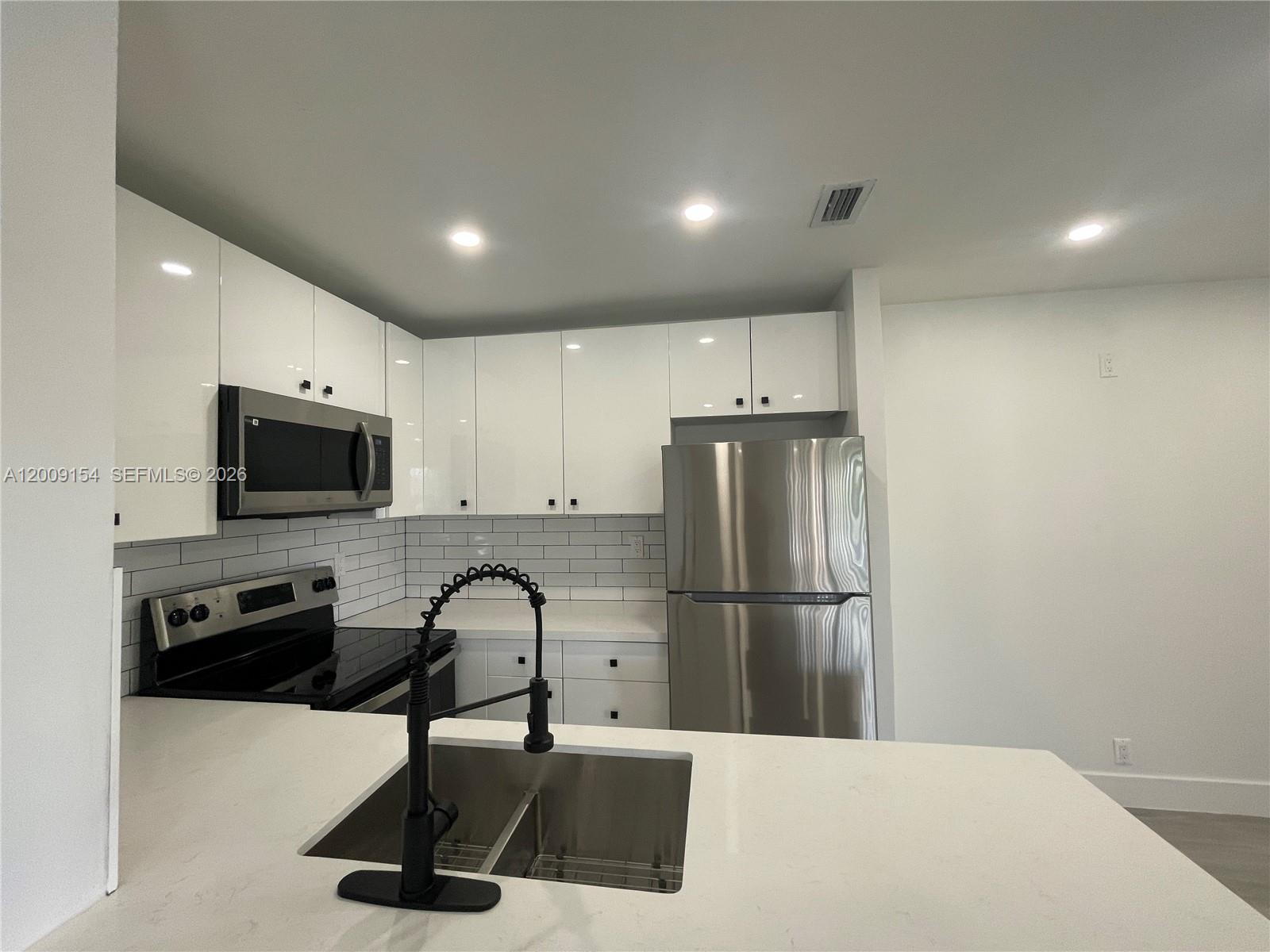 A modern kitchen features white cabinets, stainless steel appliances, a subway tile backsplash, and quartz countertops — 10016 Winding Lake Rd # 202, Sunrise FL 33351, SUNRISE, FL