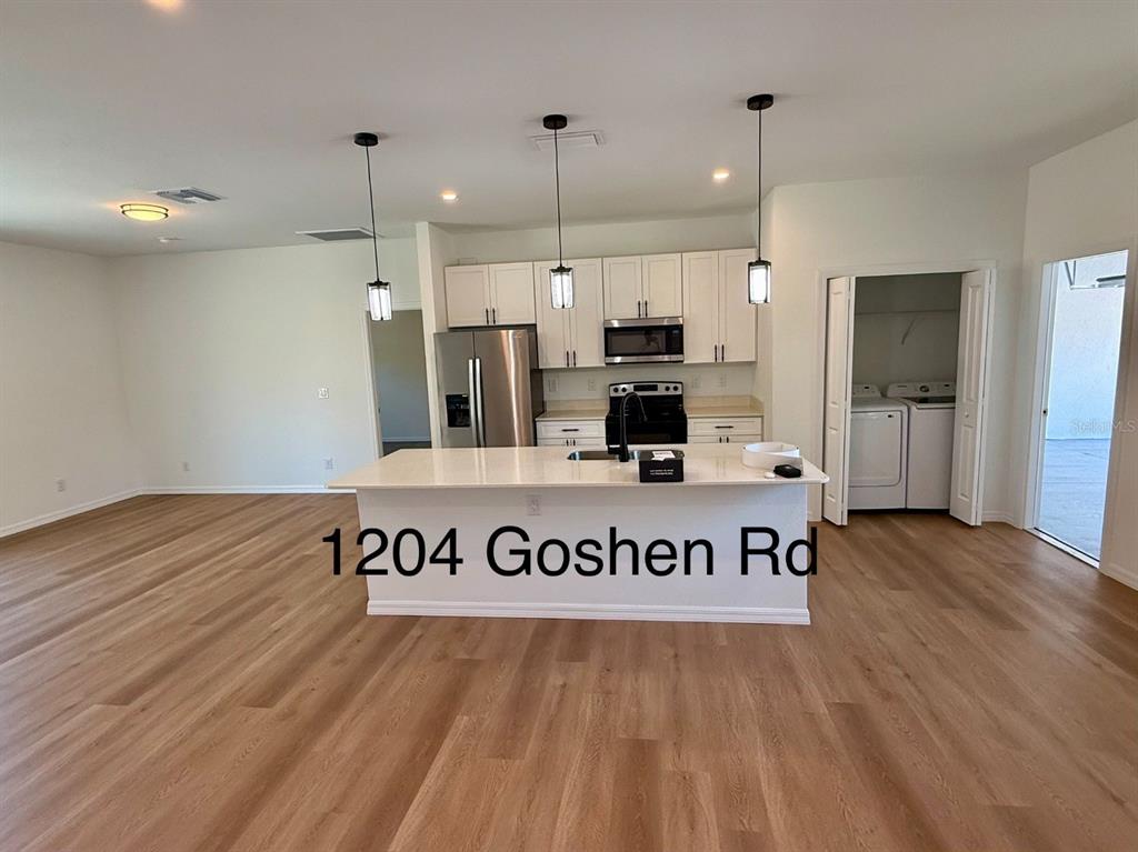 A kitchen features white cabinets, stainless steel appliances, a center island, and wood-look flooring — 1204 GOSHEN ROAD, NORTH PORT, FL