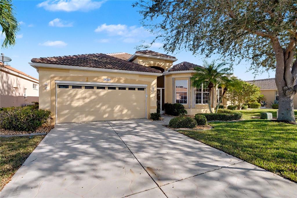A single-story house with a beige stucco exterior, a two-car garage, and a concrete driveway — 26268 FEATHERSOUND DRIVE, PUNTA GORDA, FL