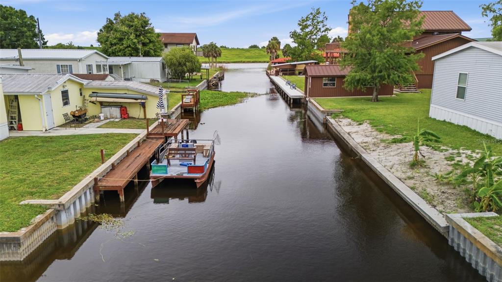 An aerial view shows a narrow canal lined with houses, docks, and a small boat — 1056 BLUE HERON LANE, MOORE HAVEN, FL