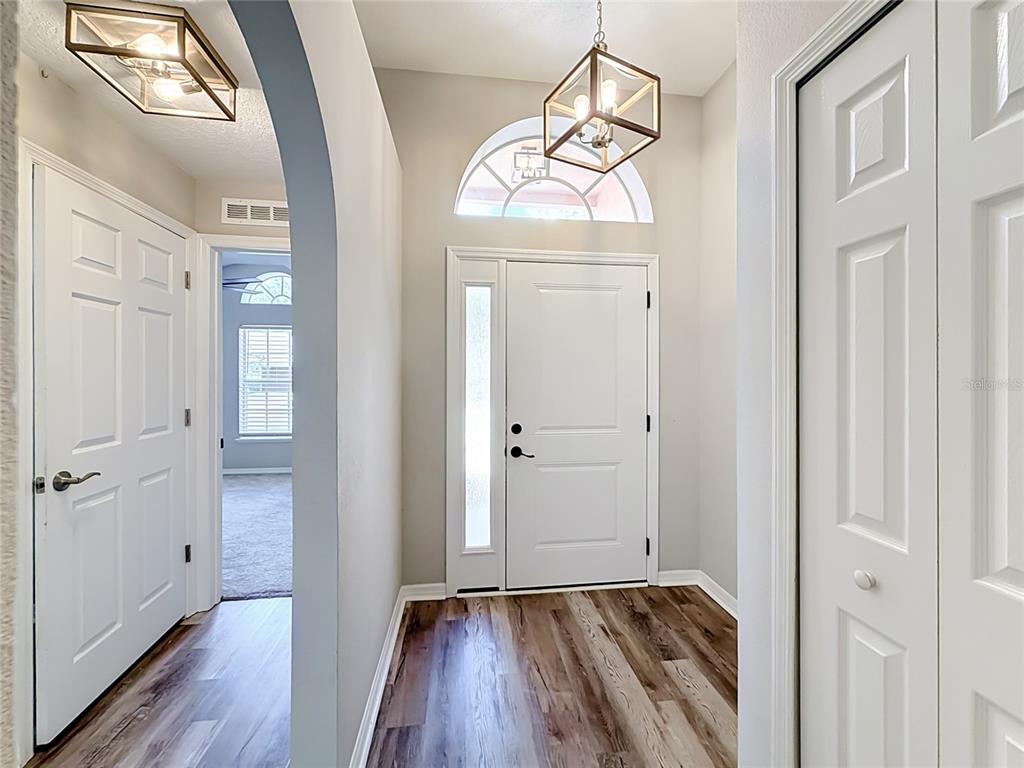 An entryway features a white front door with a sidelight, wood-look flooring, and two pendant lights — 31806 PARKDALE DRIVE, LEESBURG, FL