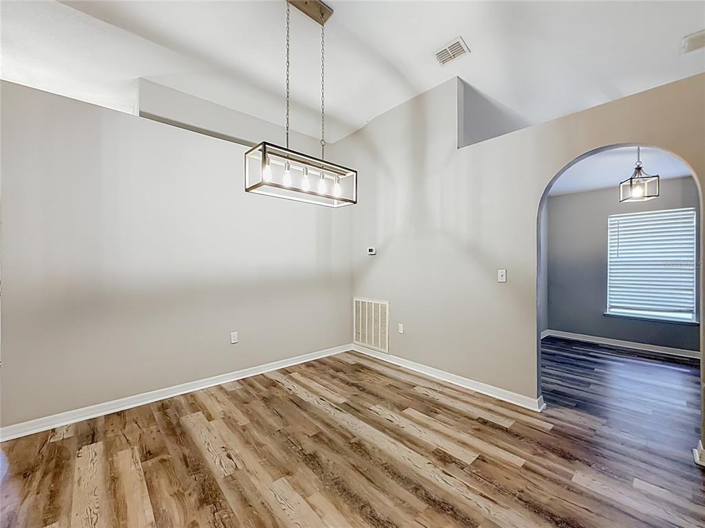 An empty dining area features wood-look flooring, a rectangular pendant light, and an arched entryway — 31806 PARKDALE DRIVE, LEESBURG, FL